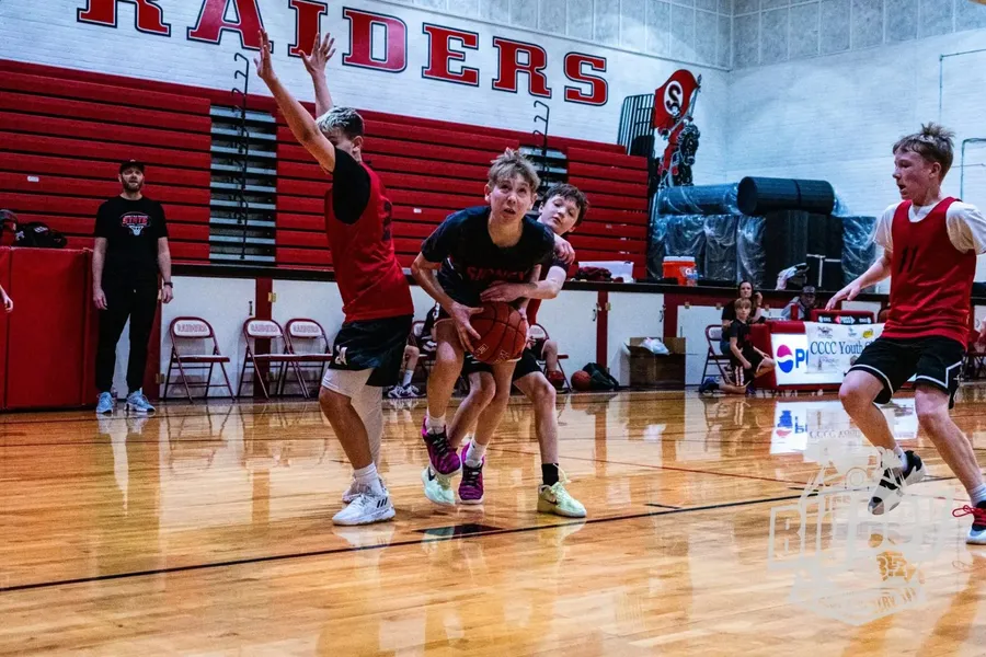 Youth basketball player in a Sidney jersey driving through two defenders during a Youth Classic tournament game